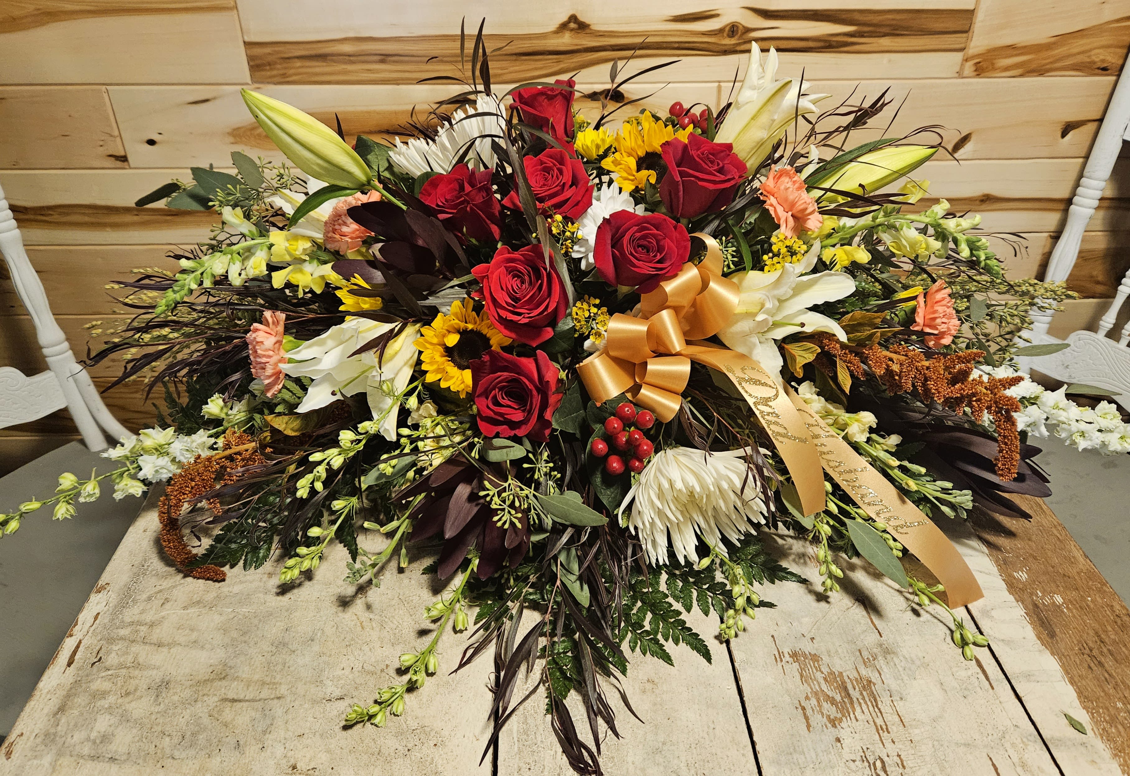 Large bouquet of red roses, white lilies, and sunflowers with a gold ribbon
