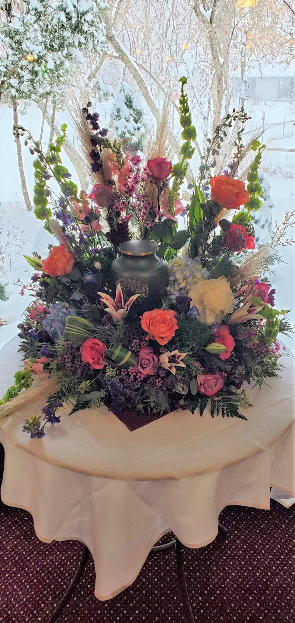 Large floral centerpiece with roses and tall mixed blooms around a black urn