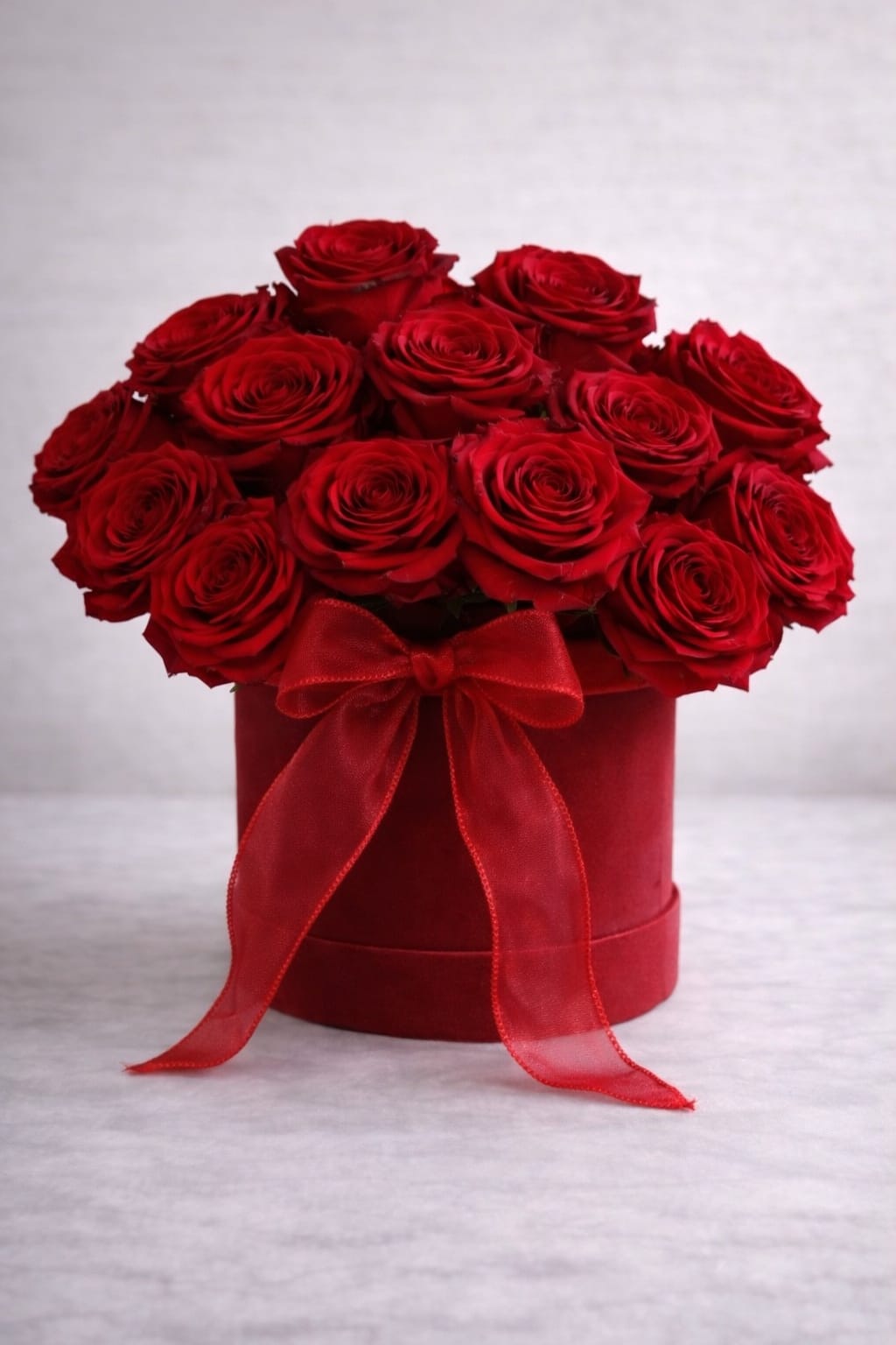Red roses arranged in a round hatbox with a red ribbon bow
