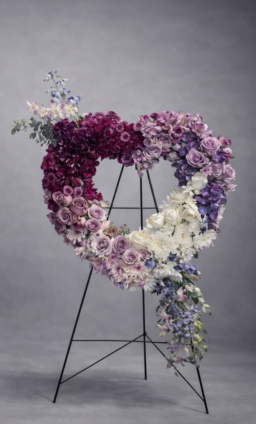 Heart-shaped floral wreath on a black stand with purple, pink, and white blooms