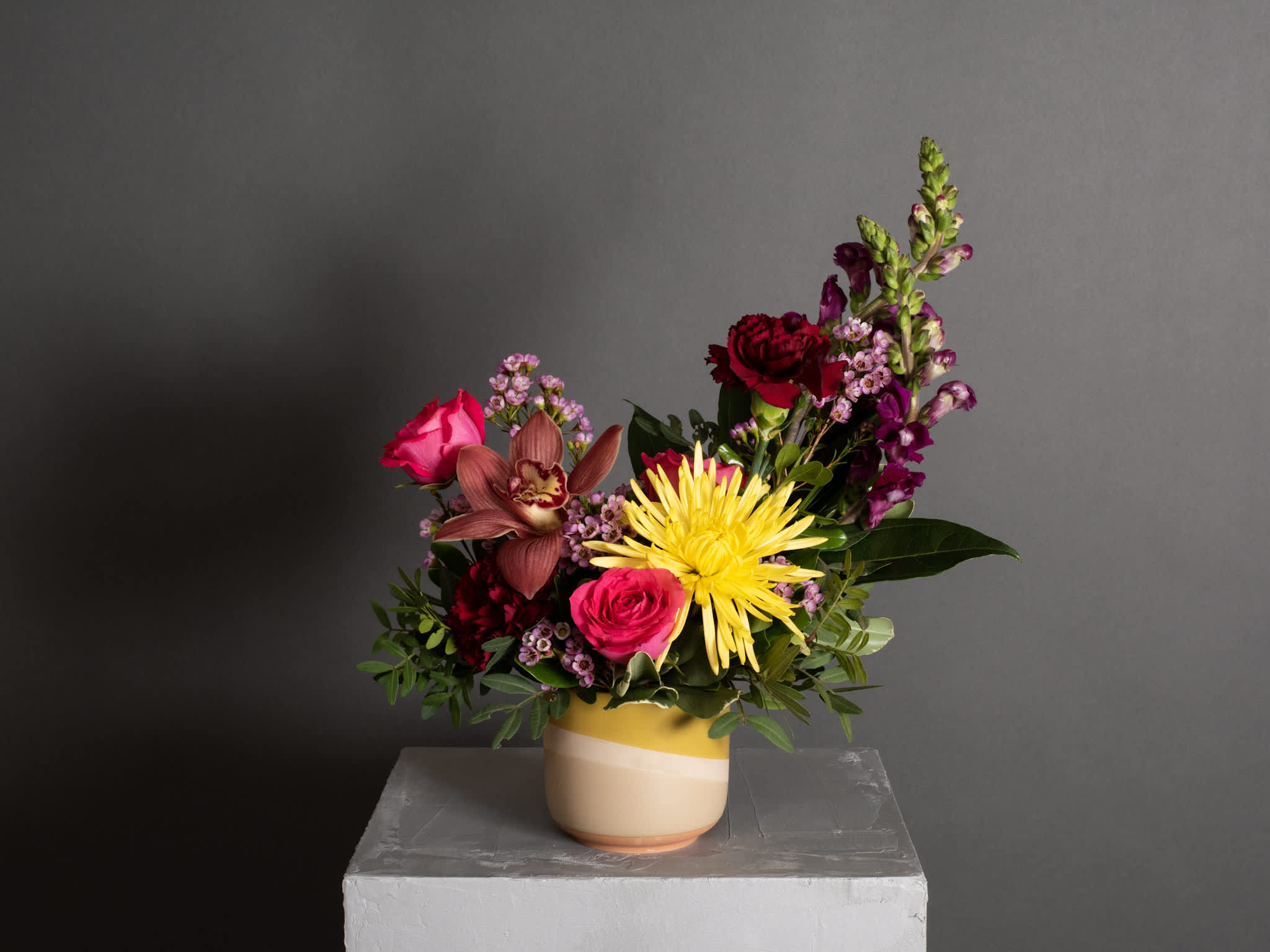 Mixed bouquet in a striped ceramic vase with pink, red, yellow, and purple blooms
