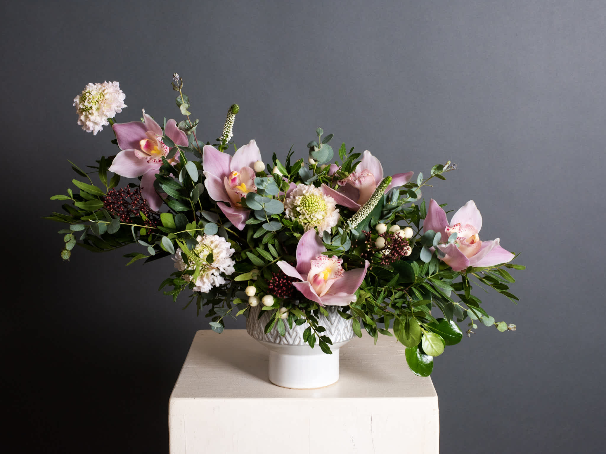 Pink orchid arrangement in a white pedestal vase