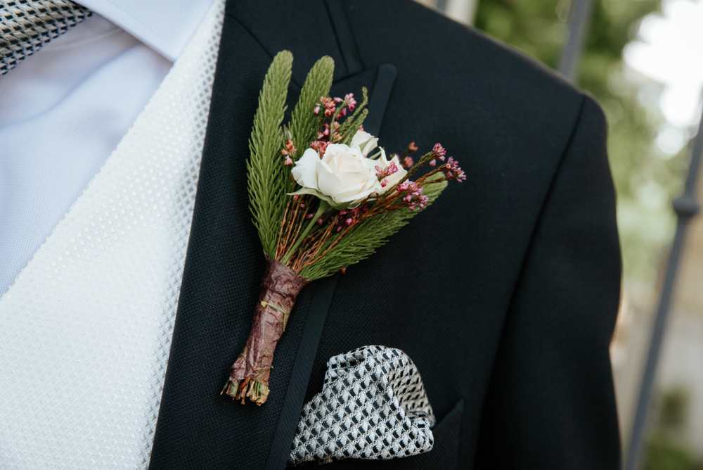 White rose boutonniere with pink filler on a suit jacket
