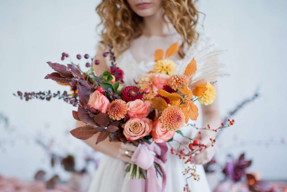 Woman holding a bouquet of peach and orange flowers with autumn leaves
