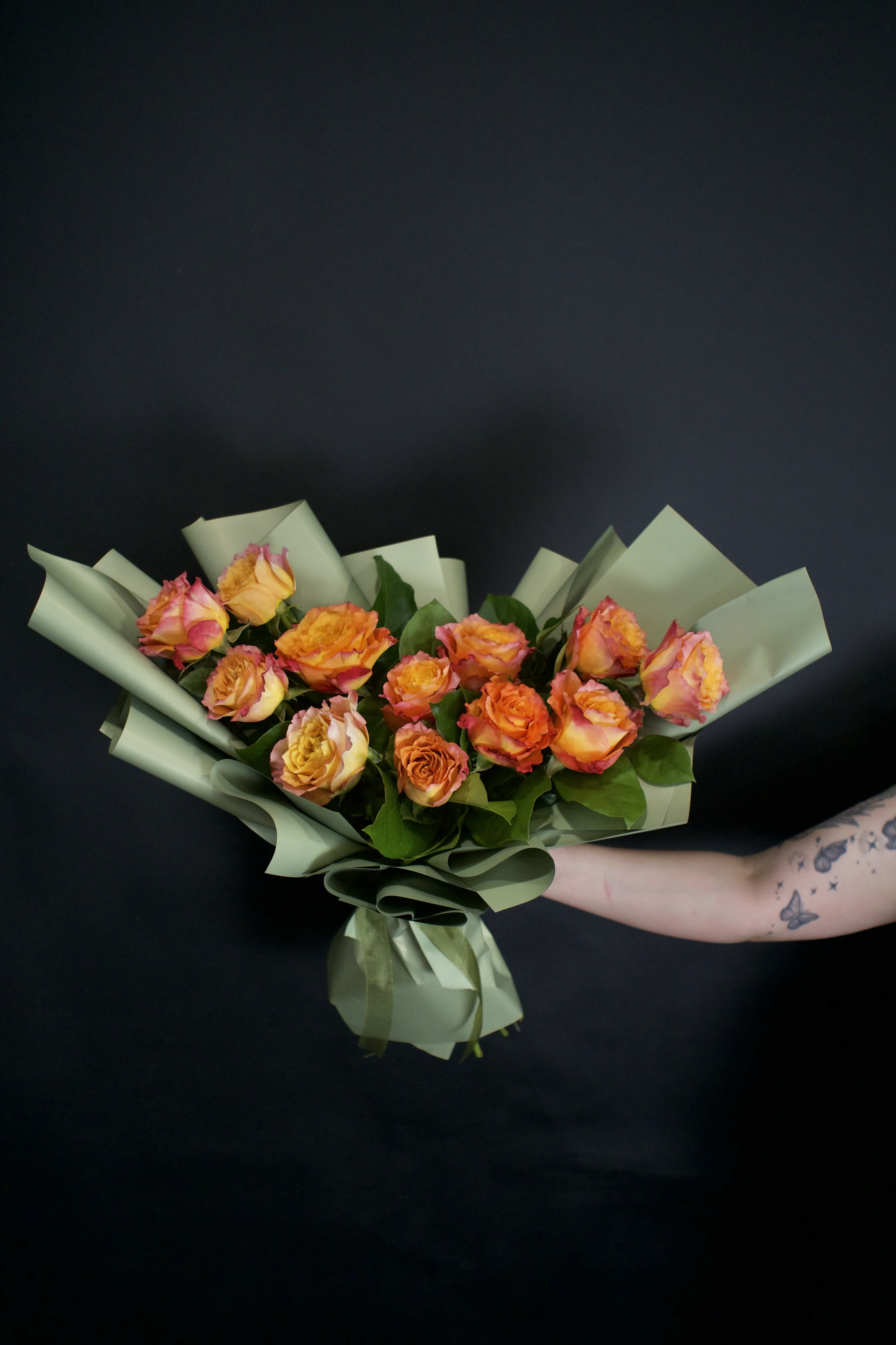 One dozen Free Spirit roses - Hand tie bouquet - A contemporary bouquet featuring twelve stunning Free Spirit roses, thoughtfully designed with a modern aesthetic. Known for their breathtaking blend of warm peach, apricot, orange, and soft pink tones, Free Spirit roses bring exceptional beauty and character to this elegant hand-tied bouquet. Wrapped in premium sage green paper and complemented by lush greenery, each bouquet is finished with a luxurious ribbon for a polished presentation.  One of the most beloved specialty roses, Free Spirit roses are prized for their large, beautifully ruffled blooms that continue to open dramatically over time, revealing layers of colour and texture. Their delightful fragrance adds another layer of beauty, making this bouquet as captivating to smell as it is to admire.  Sophisticated, romantic, and full of character, this bouquet makes a memorable gift for birthdays, anniversaries, celebrations, or simply because.