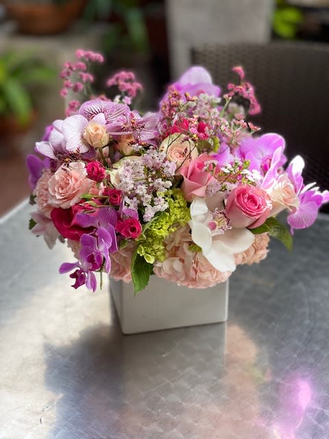 Pink and purple mixed flower arrangement in a white square vase