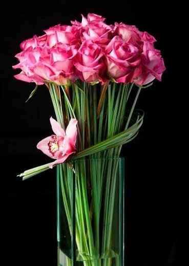 Pink roses arranged in a tall glass vase with one orchid bloom
