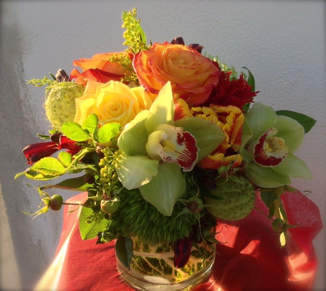 Bouquet of orange and yellow roses with green orchids in a glass vase