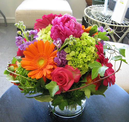 Bright mixed bouquet in a clear glass vase with pink, orange, purple, and green blooms.