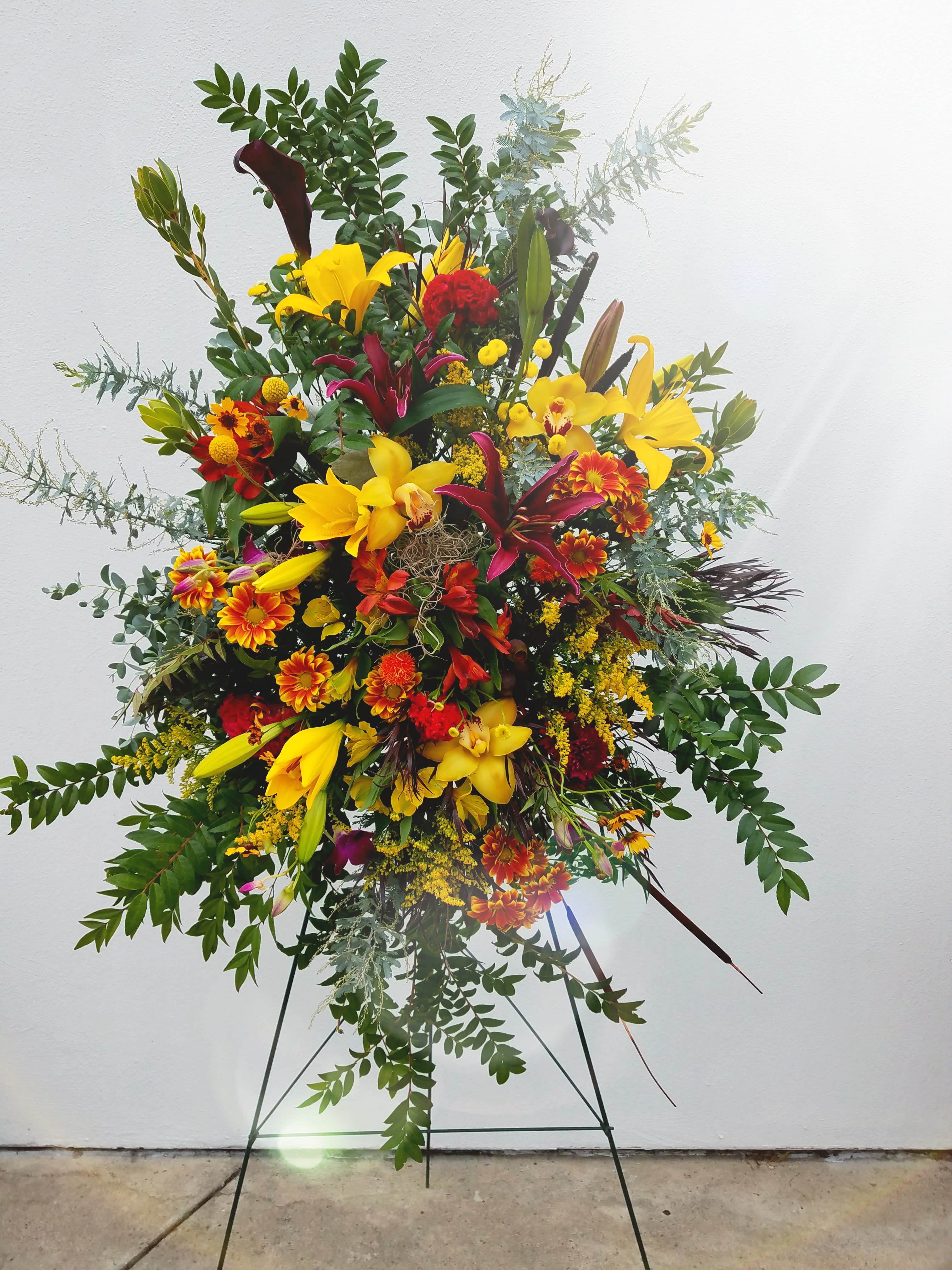 Large standing floral spray with yellow lilies and red-orange blooms