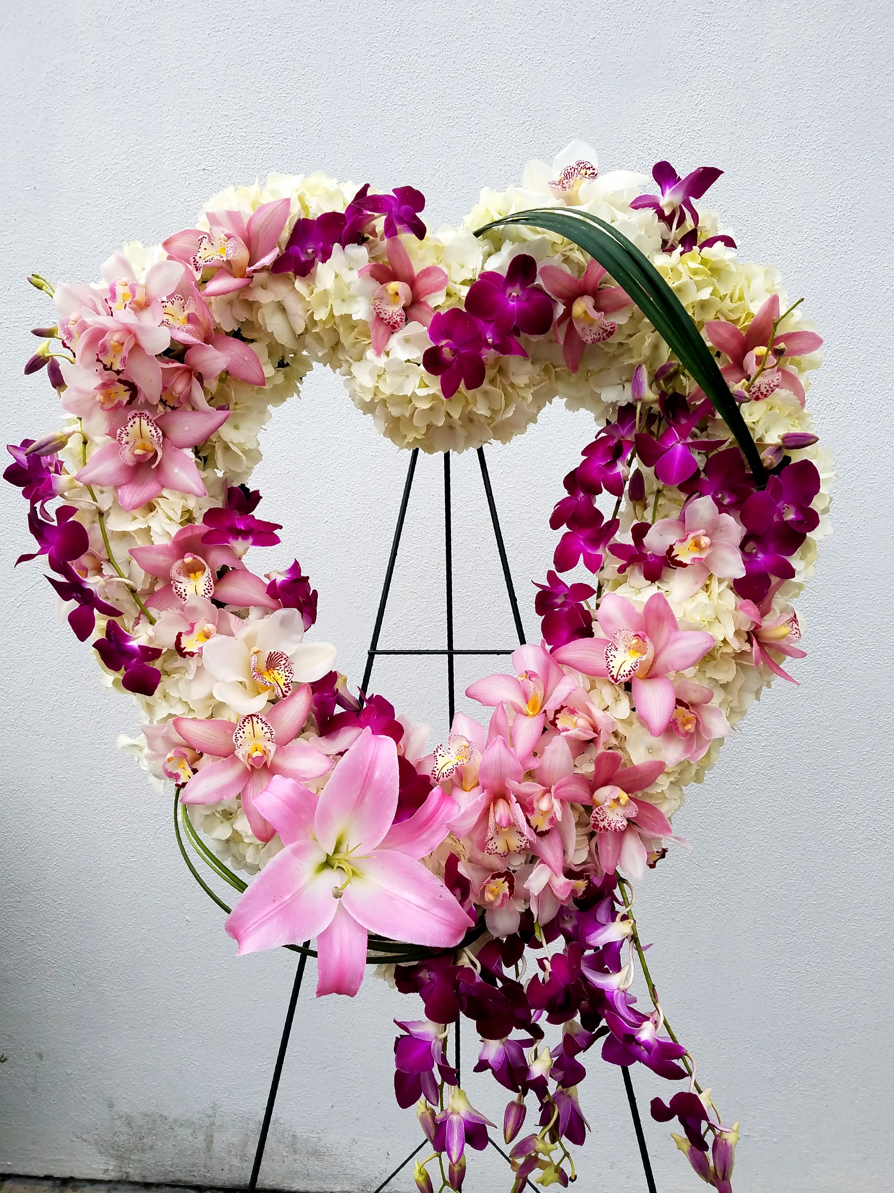 Heart-shaped floral wreath with pink and purple orchids on a stand