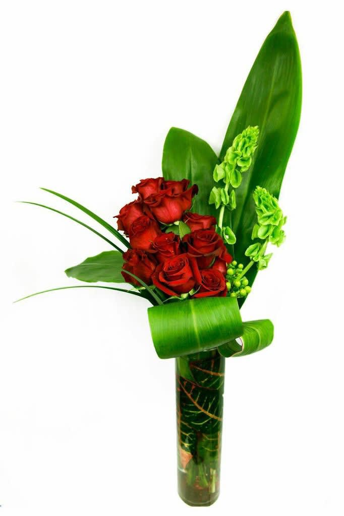 Red roses arranged with green leaves in a tall glass vase