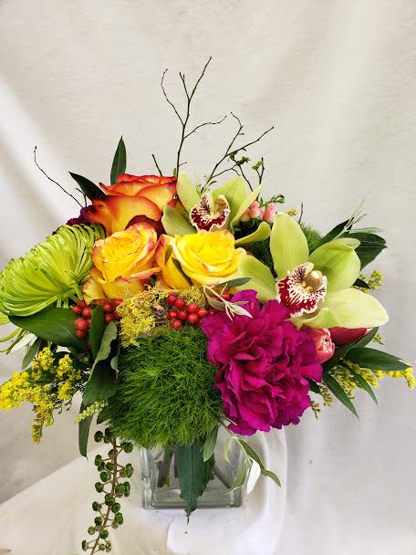 Bright mixed bouquet with roses, orchids, and a glass vase