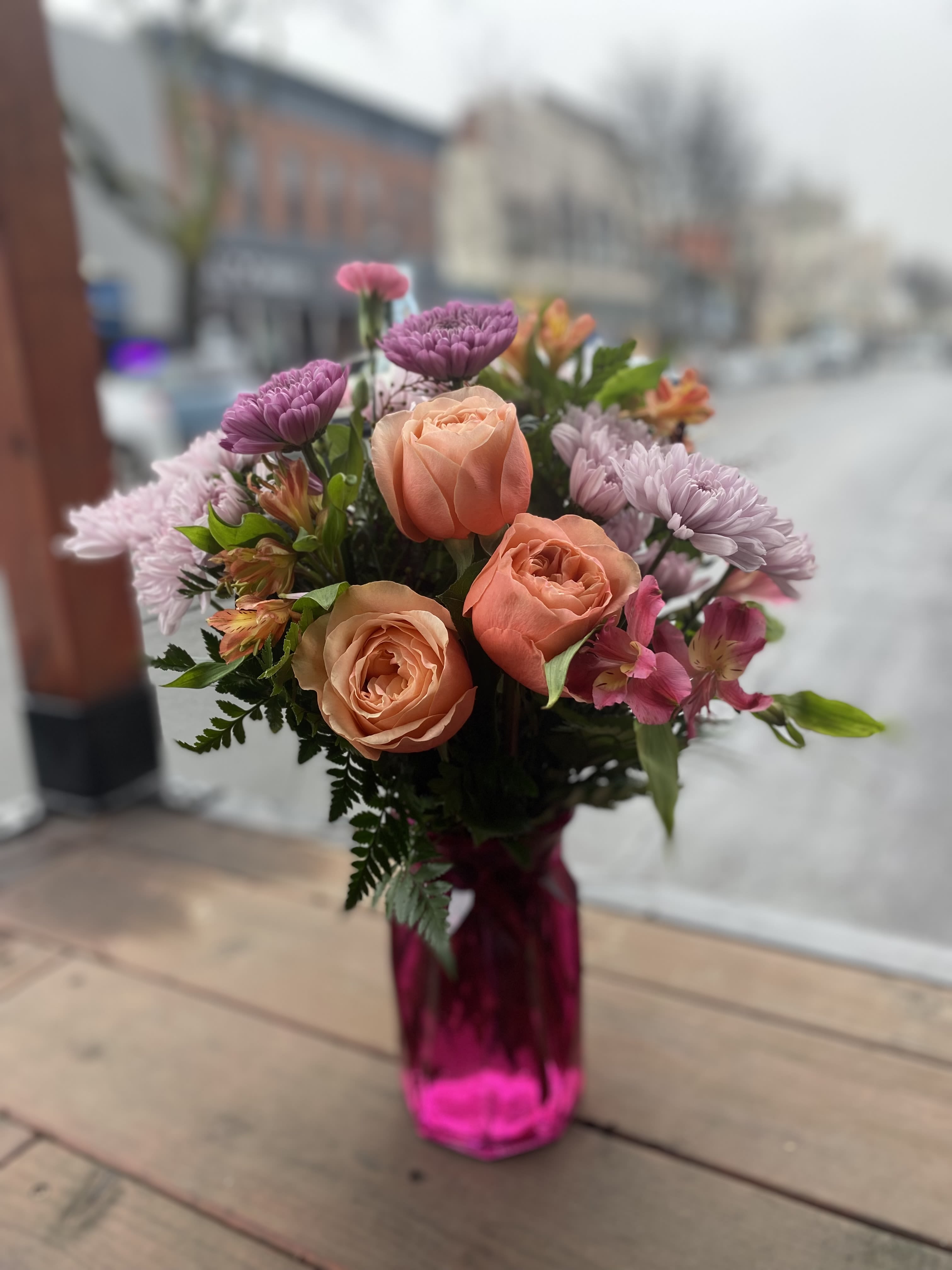 Bouquet of peach roses and purple flowers in a pink glass vase