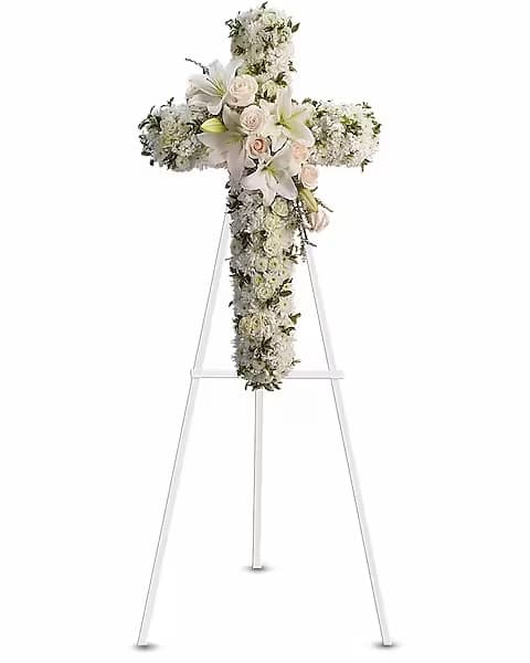 White floral cross arrangement on a stand with lilies and roses