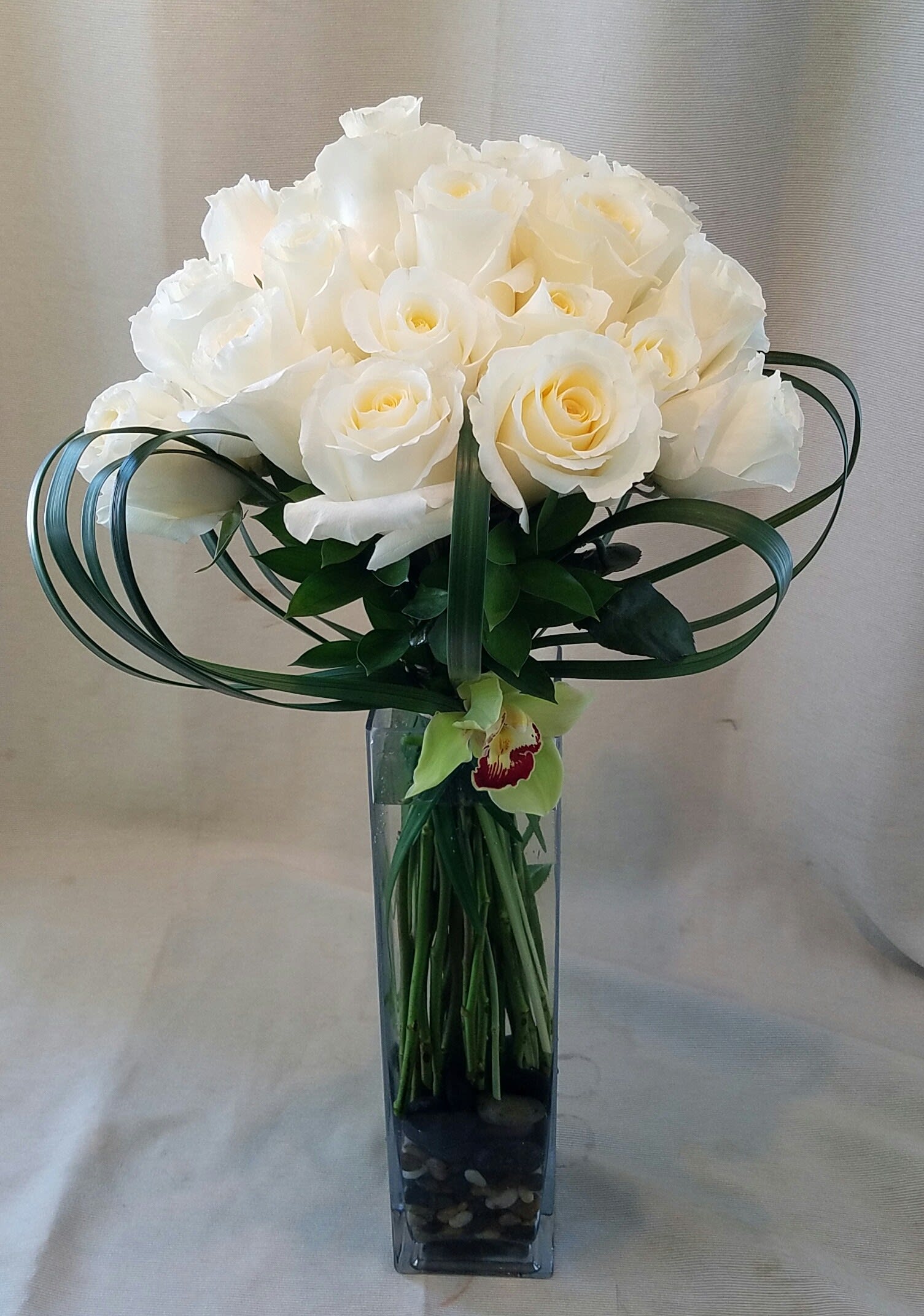 White rose bouquet in a tall glass vase with looping green leaves