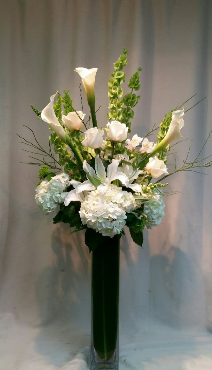 White calla lilies and hydrangeas in a tall glass vase