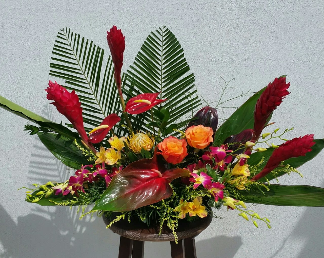 Tropical floral arrangement with red ginger, orchids, and orange roses in a low container