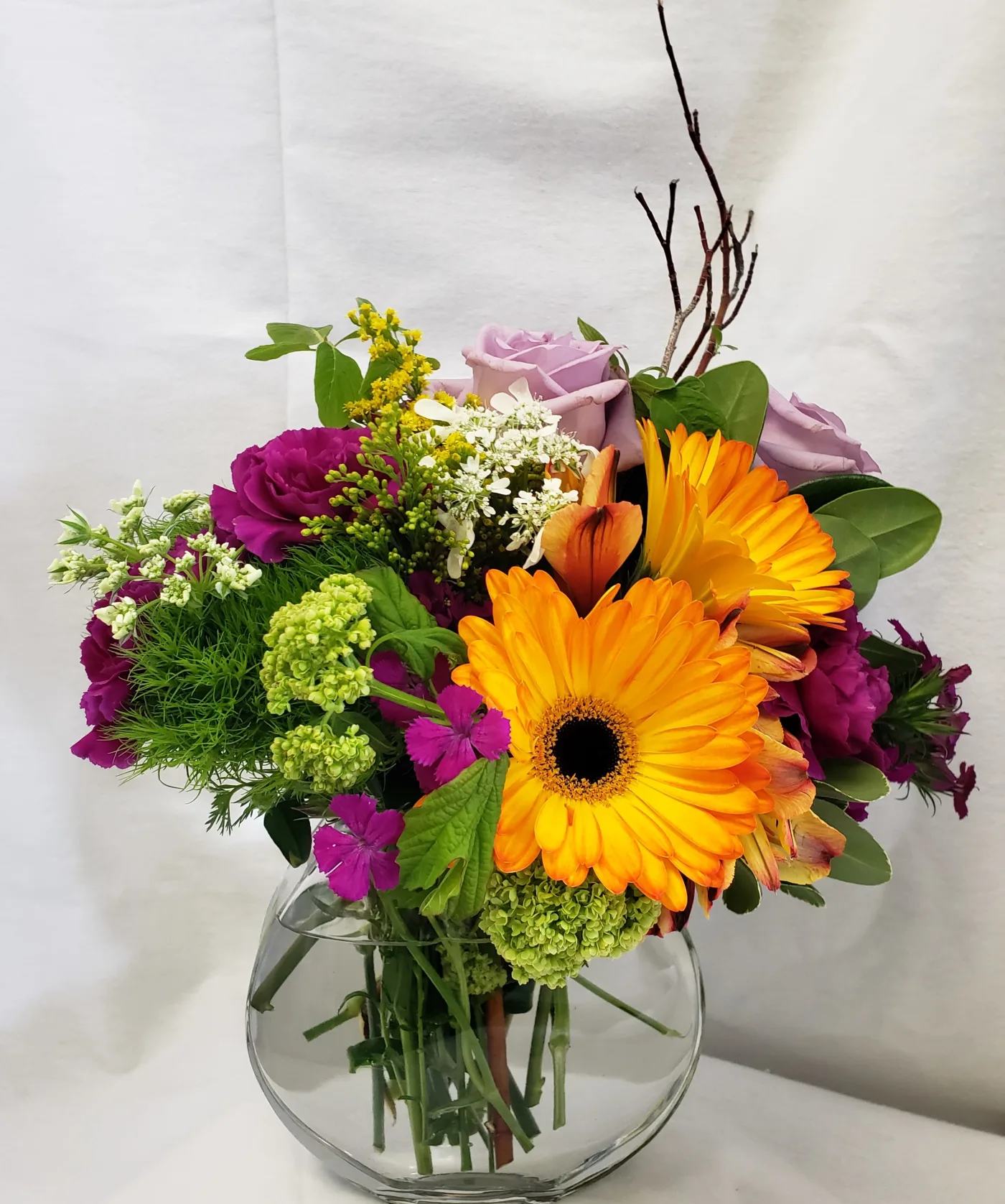 Colorful bouquet with orange gerbera daisies and lavender roses in a glass vase