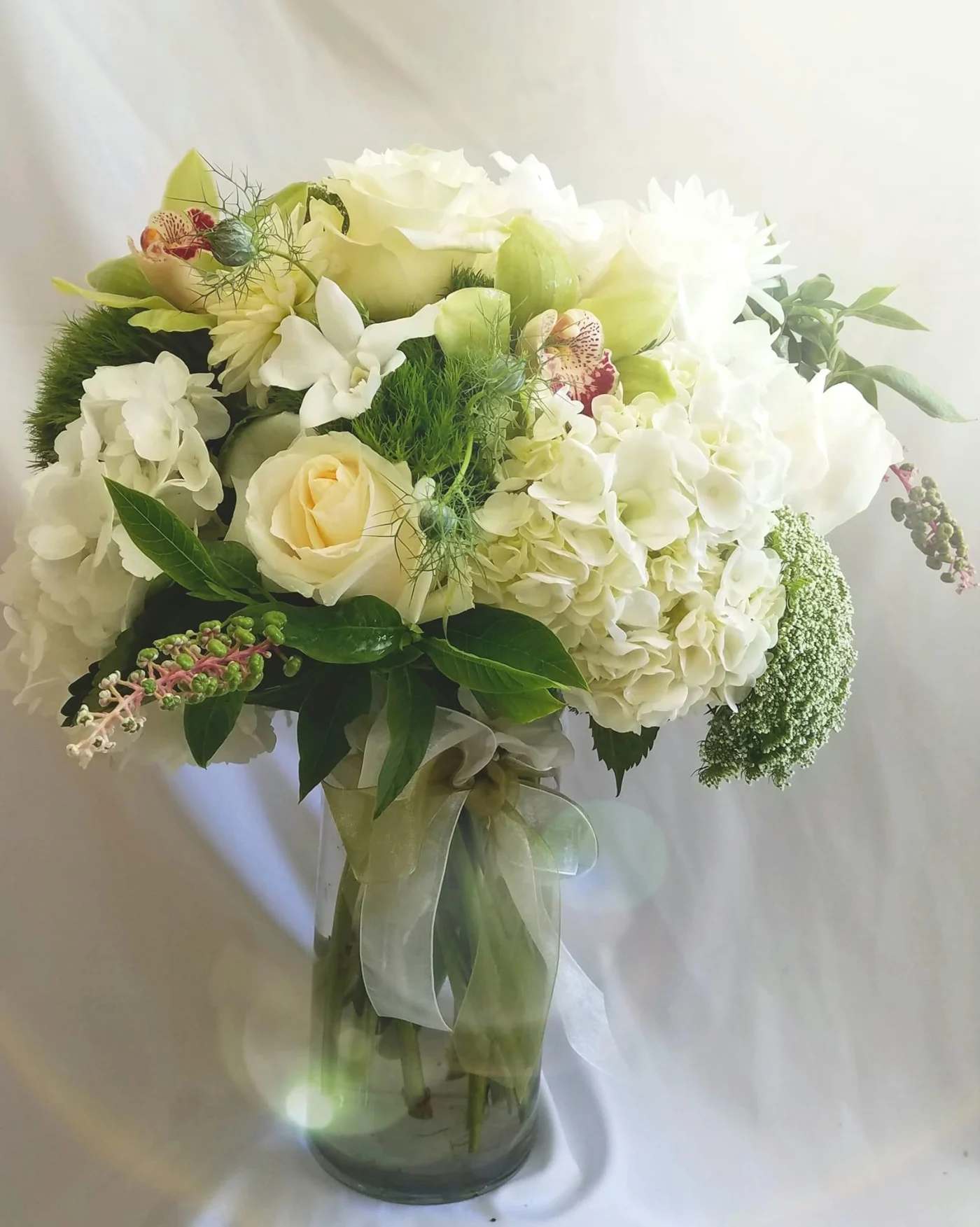 White and pale green bouquet in a glass vase with ribbon