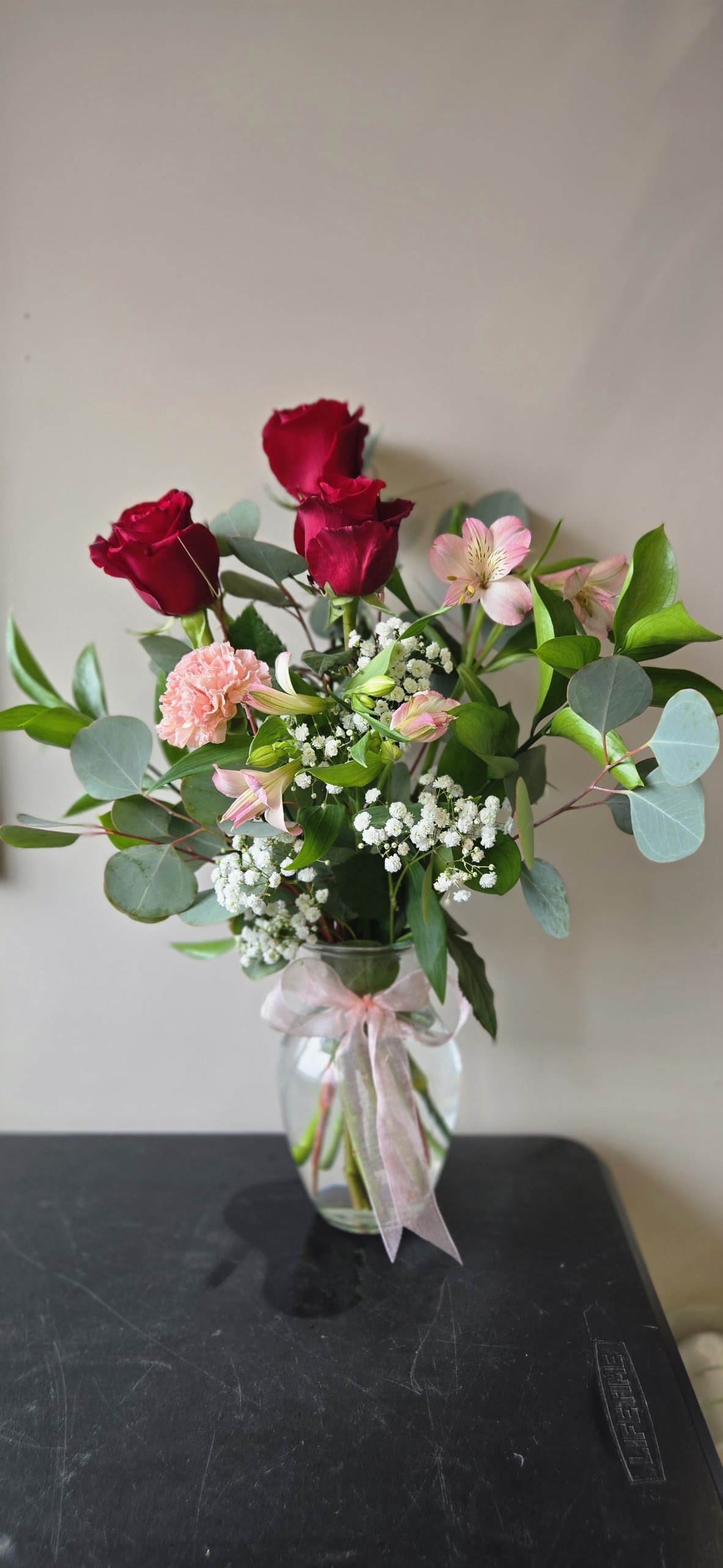 Bouquet of red roses and pink flowers in a glass vase with a ribbon
