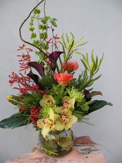 Tall tropical arrangement with orchids and calla lilies in a glass vase