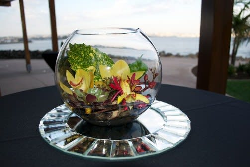 Glass bowl with yellow orchids and red flowers on a mirrored base