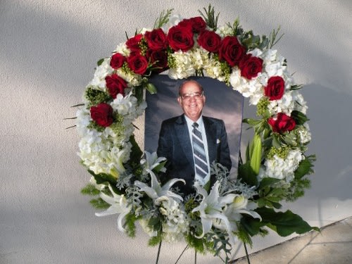 Floral funeral wreath with red roses and white lilies around a framed portrait