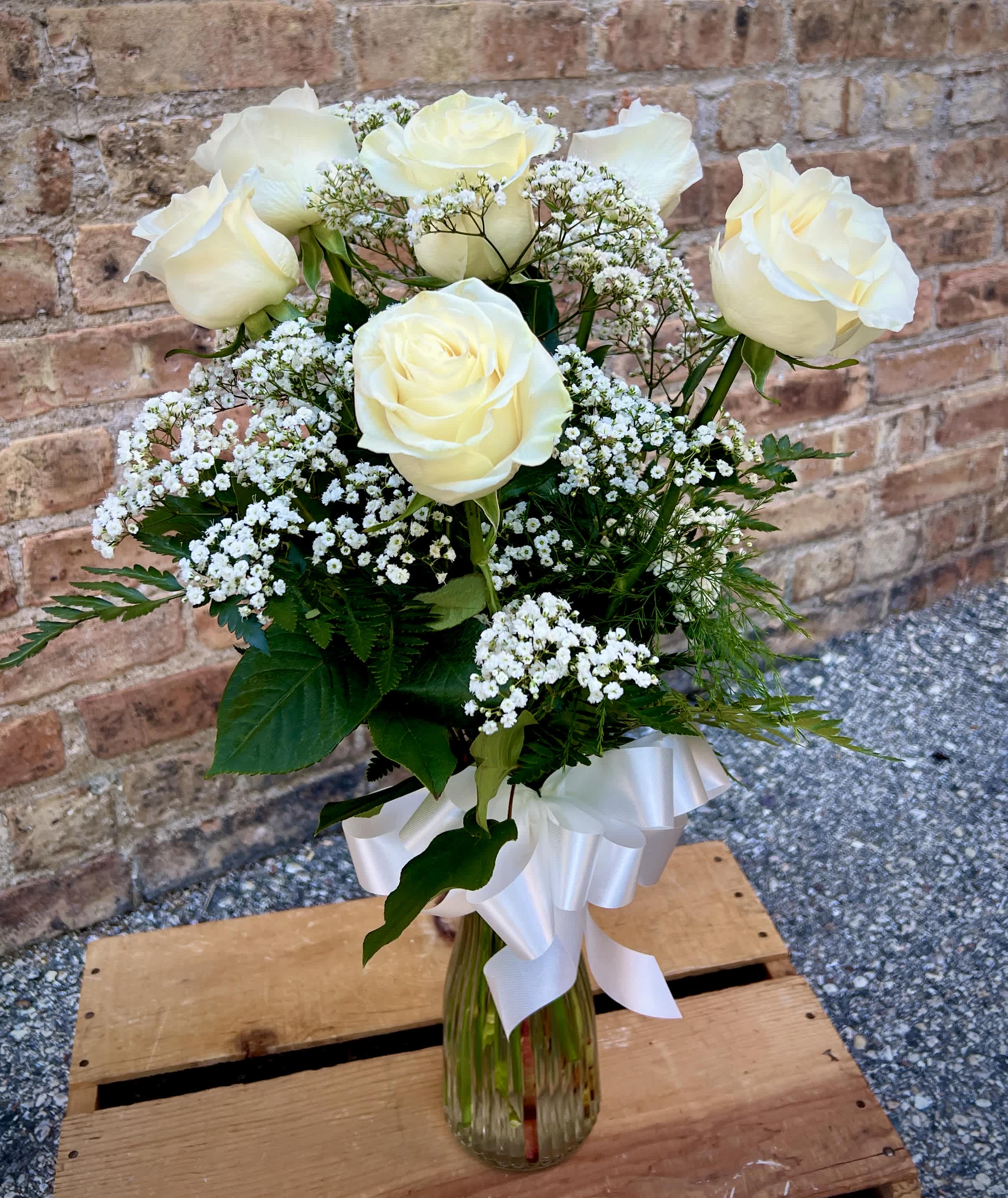 White roses and baby's breath in a clear glass vase with a white ribbon