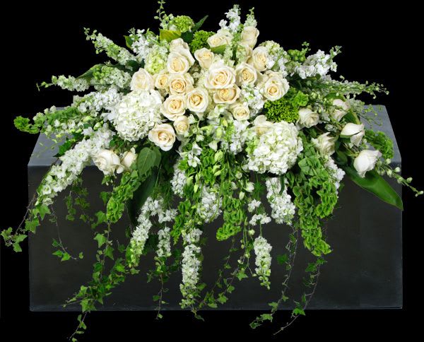 White rose and hydrangea arrangement with trailing greenery on a dark pedestal