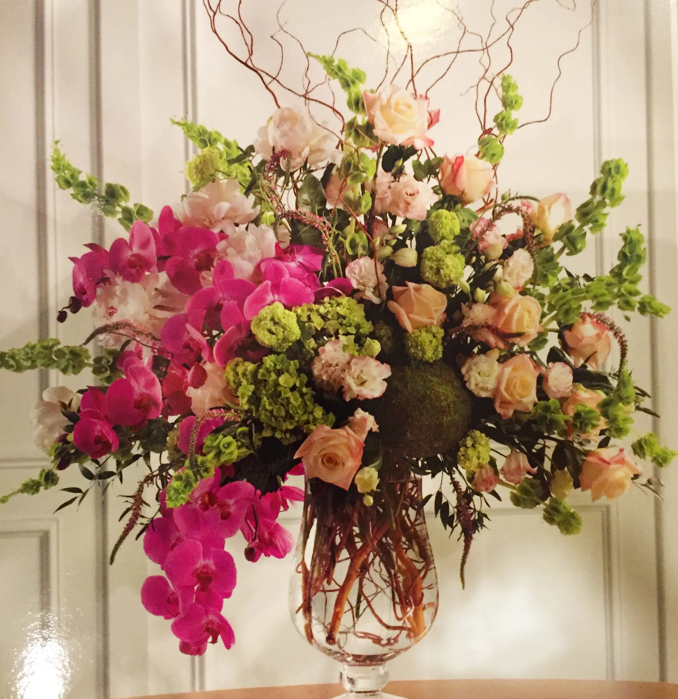 Large floral arrangement in a glass vase with pink orchids and peach roses