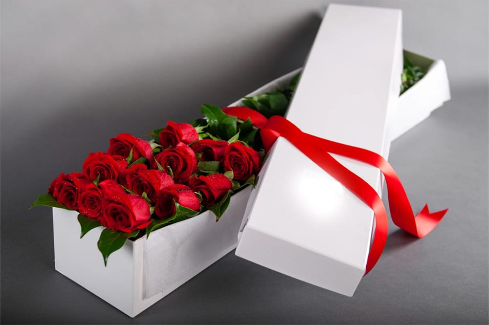 Red roses arranged in a white gift box with a red ribbon