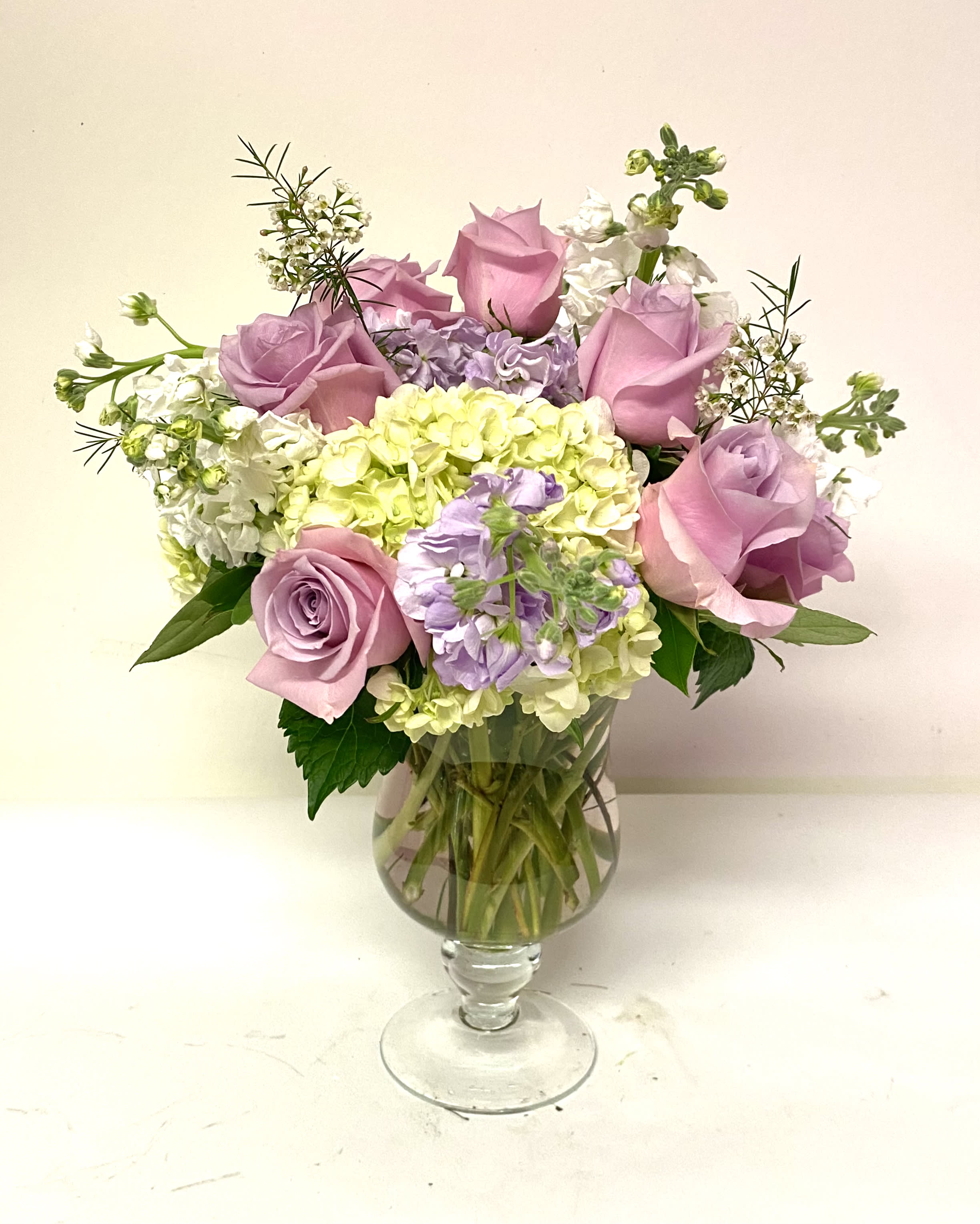 Pink roses and pastel hydrangeas arranged in a clear glass vase