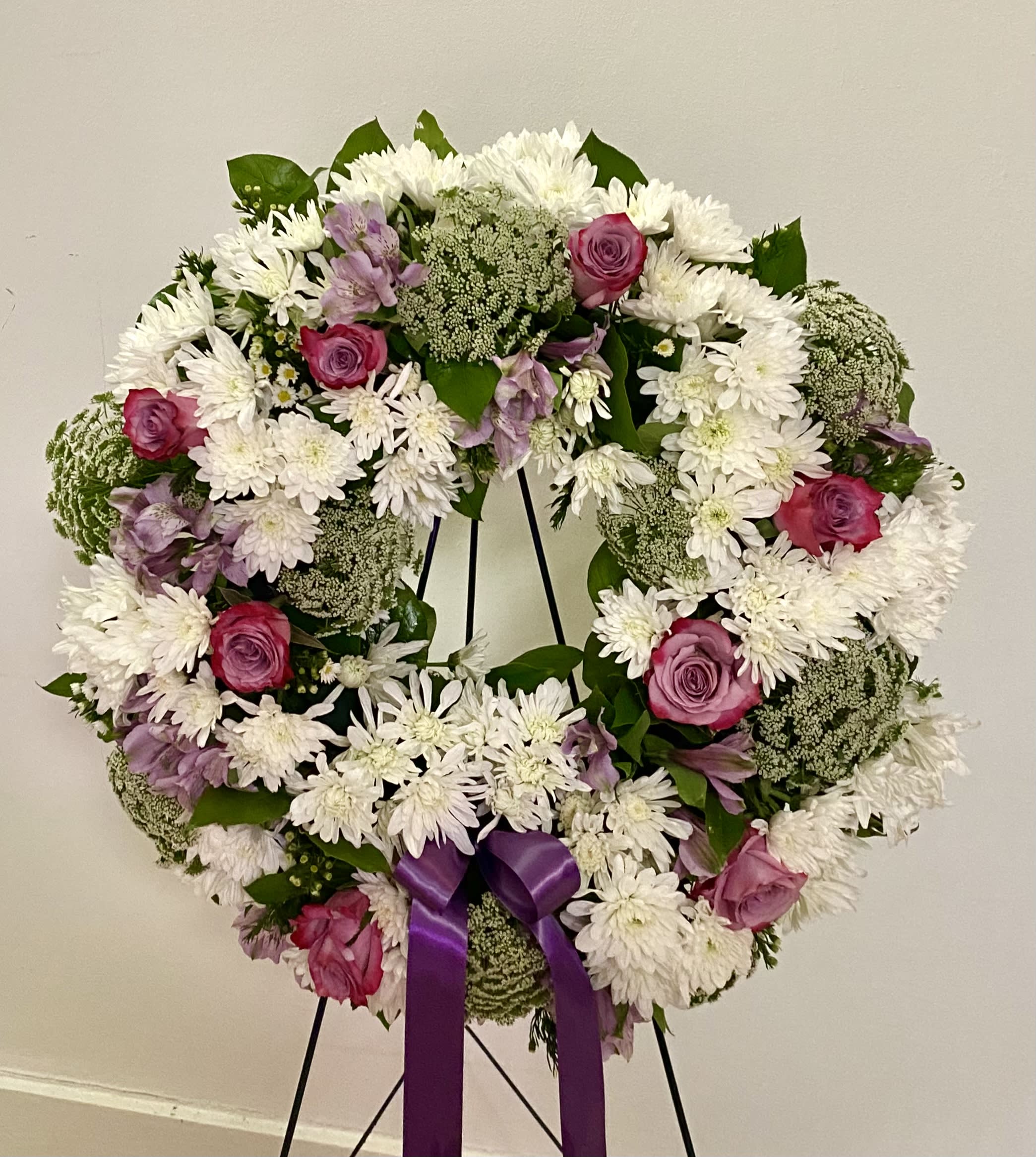 Round floral wreath with white daisies, pink roses, and a purple ribbon