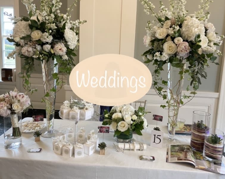 Wedding table with tall white floral arrangements and a glowing "Weddings" sign