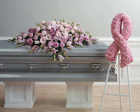 Pink floral casket spray on a gray casket beside a pink ribbon wreath