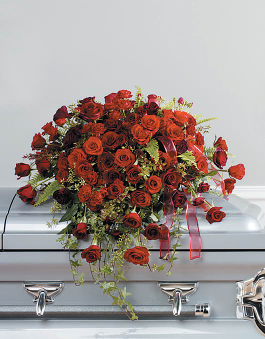 Red rose casket spray with trailing greenery and ribbon
