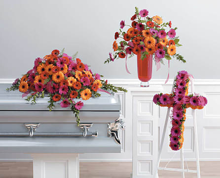 Bright gerbera daisy funeral arrangements on a casket and easel cross.