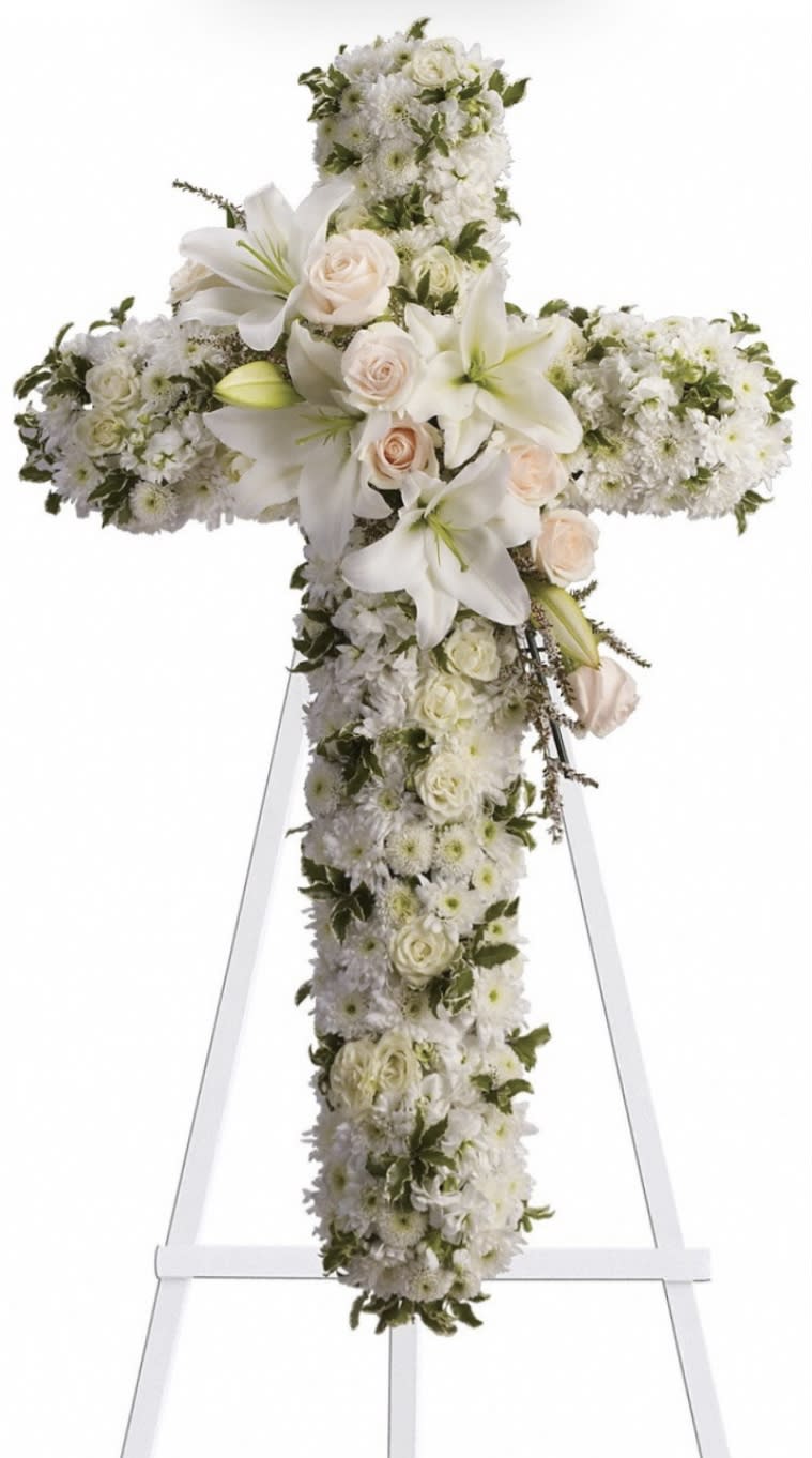 White floral cross on an easel with roses and lilies