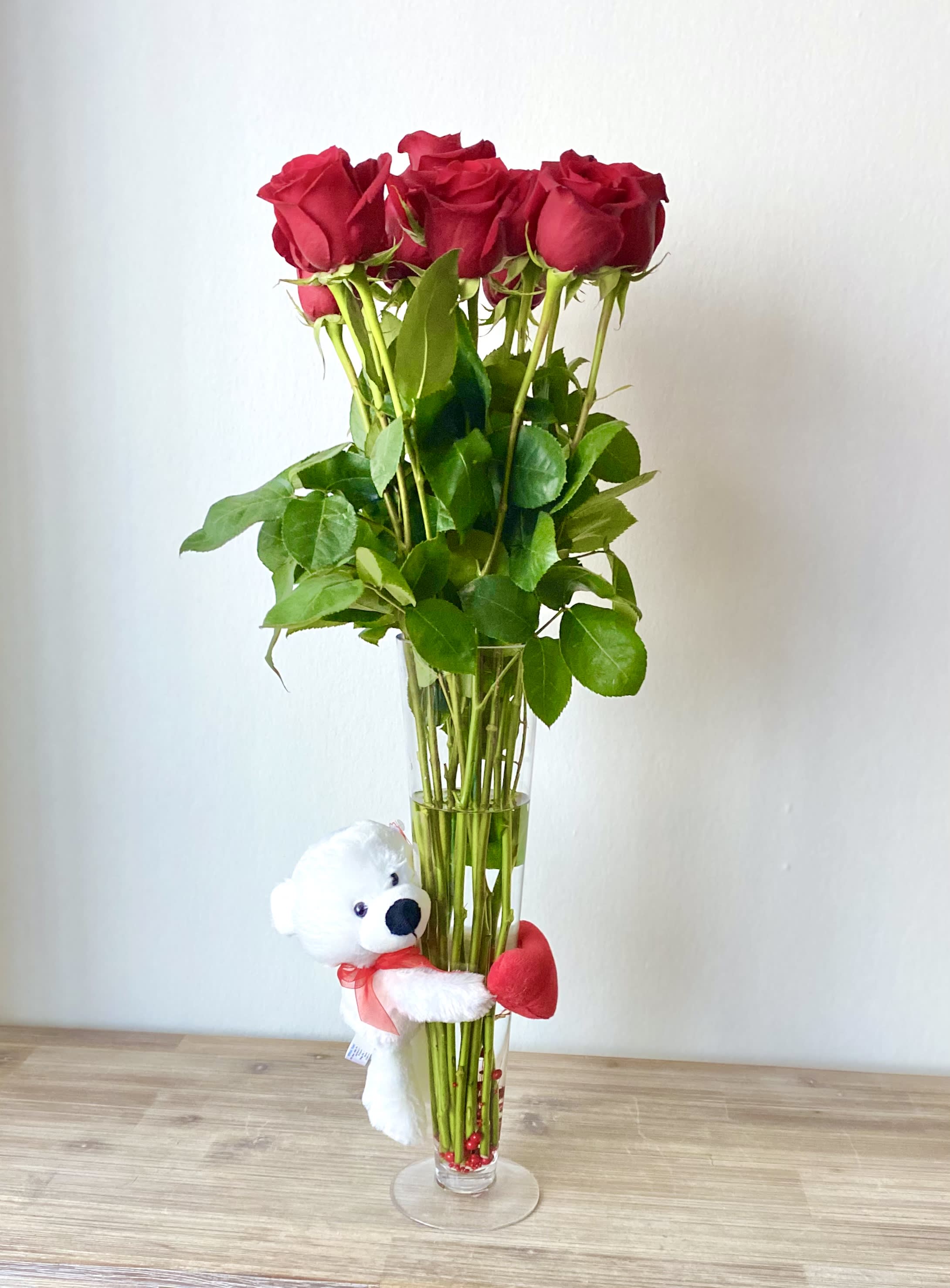 Red roses in a tall glass vase with a small teddy bear attached