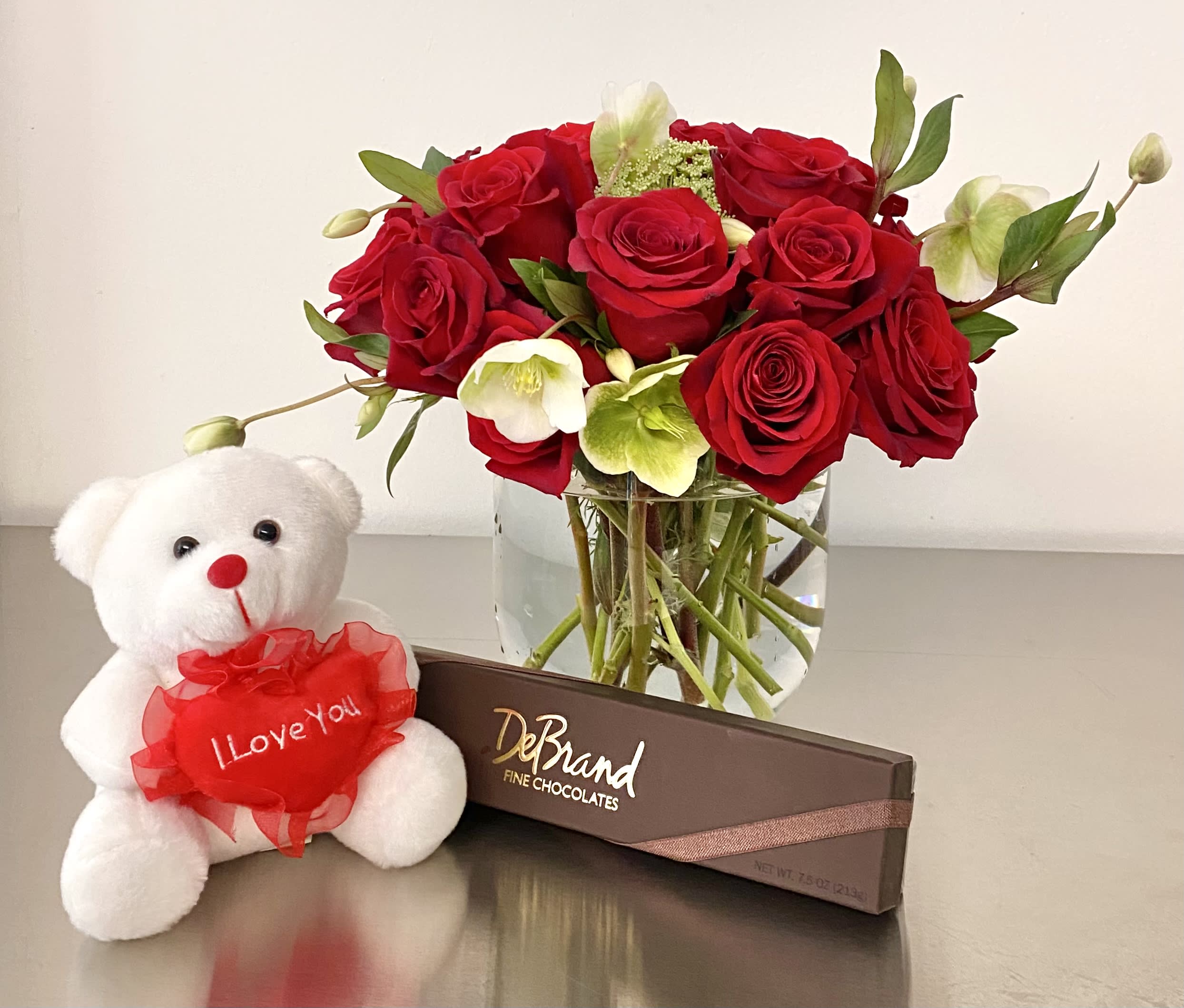 Red roses in a glass vase with a teddy bear and chocolate box