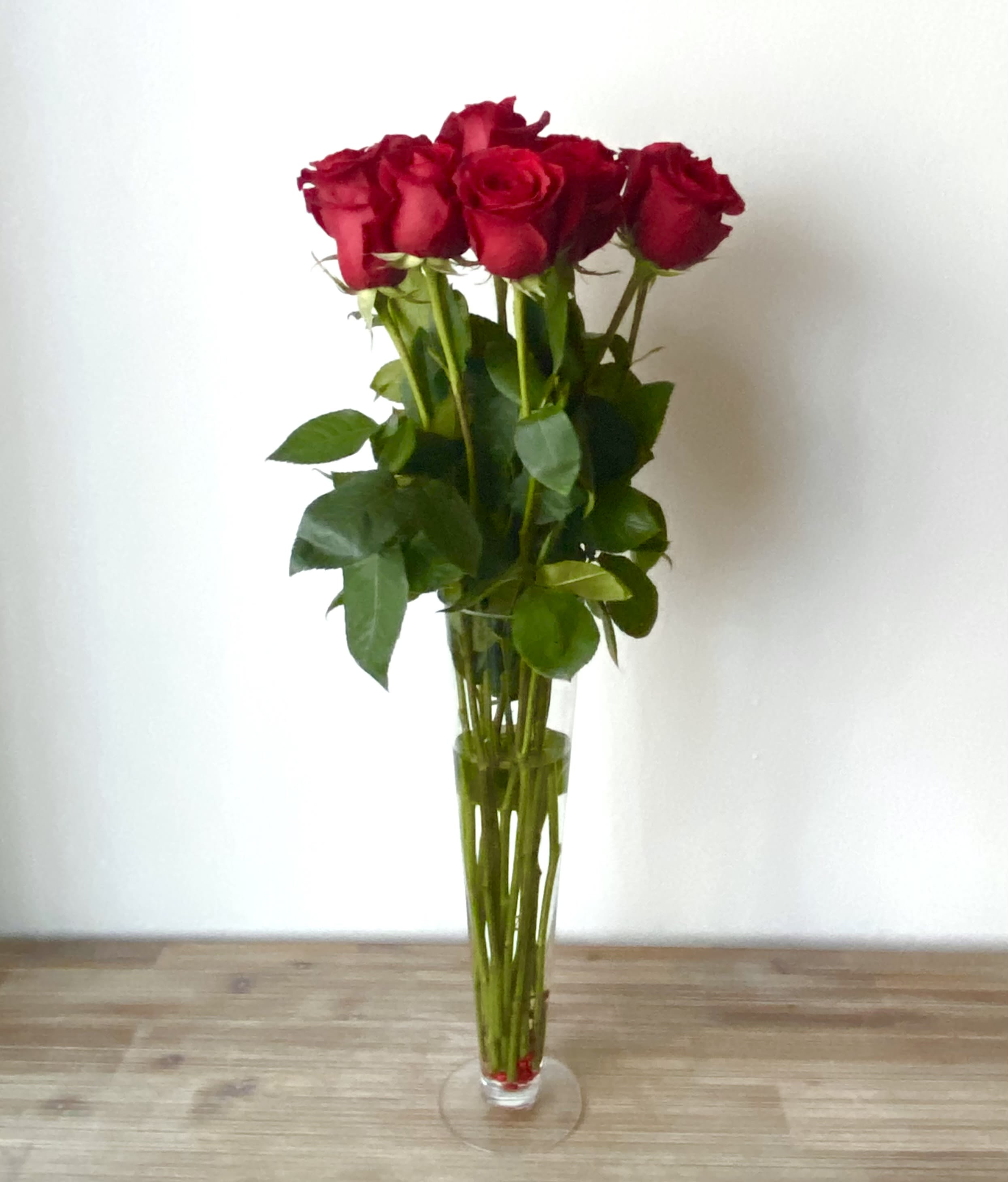 Tall vase of red roses with green foliage