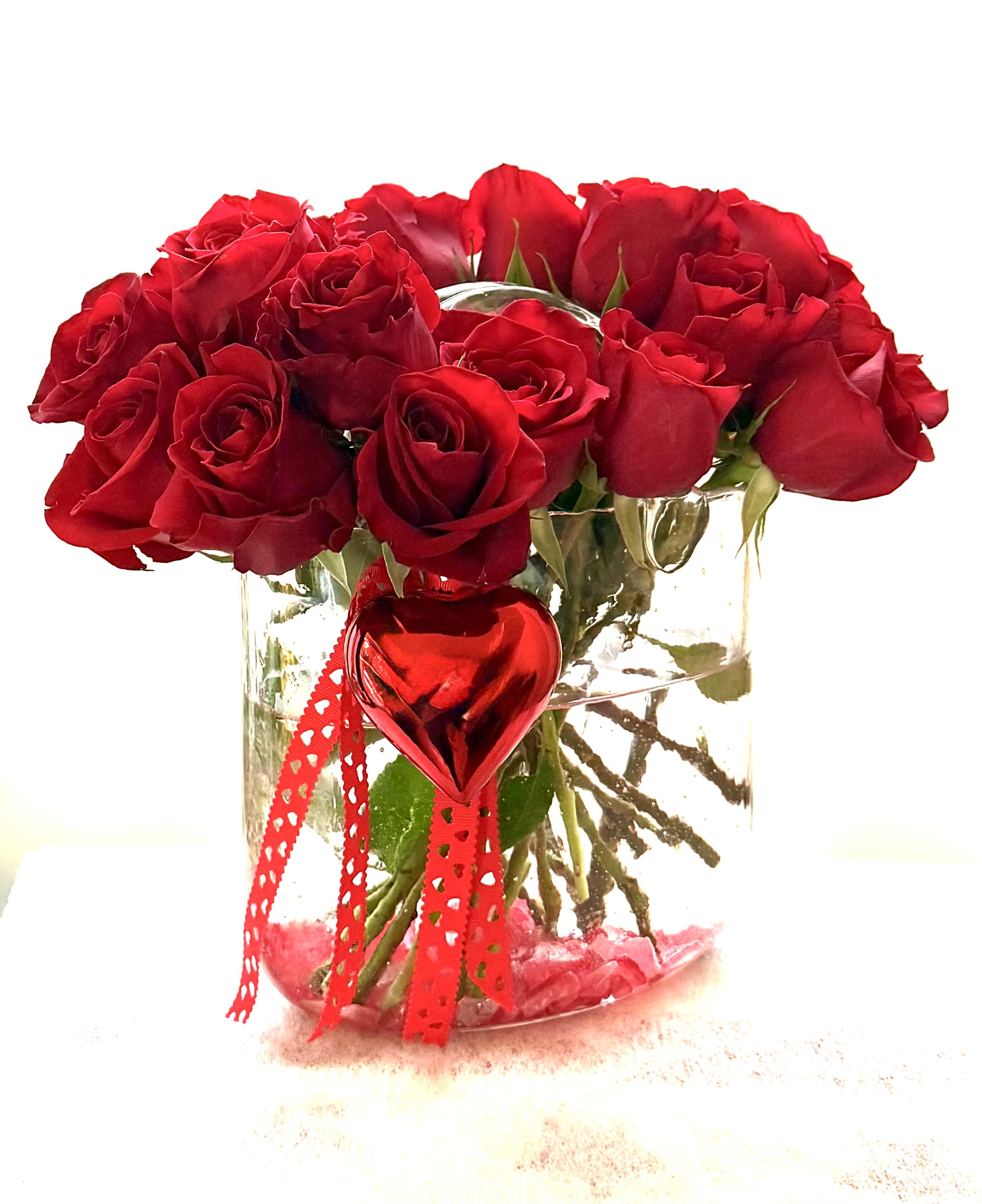 Red roses in a clear glass vase with a red heart ornament and ribbon
