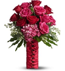 Bouquet of red and pink roses with greenery in a red satin-wrapped vase