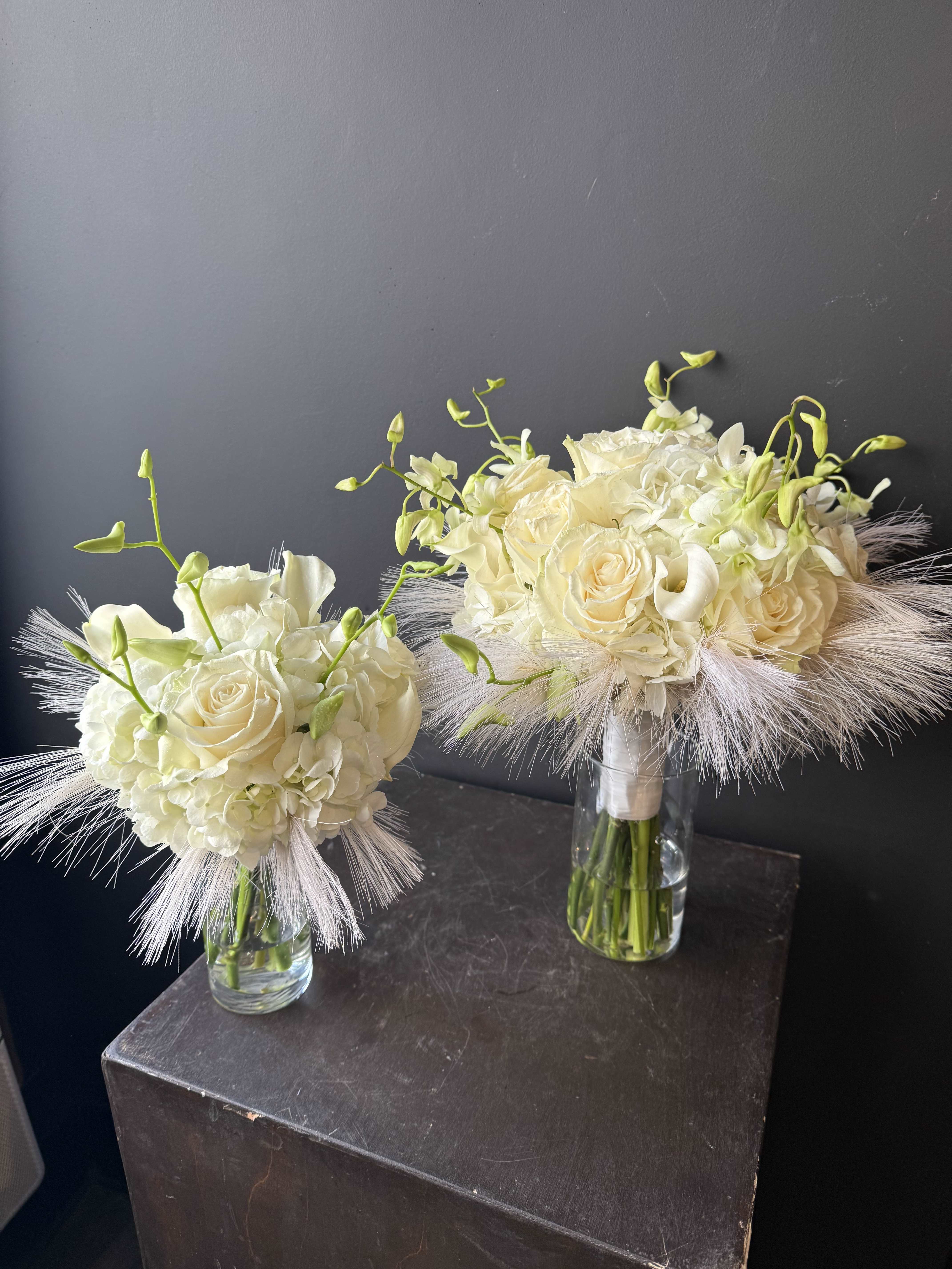 Two ivory bridal bouquets in clear glass vases with feathery accents