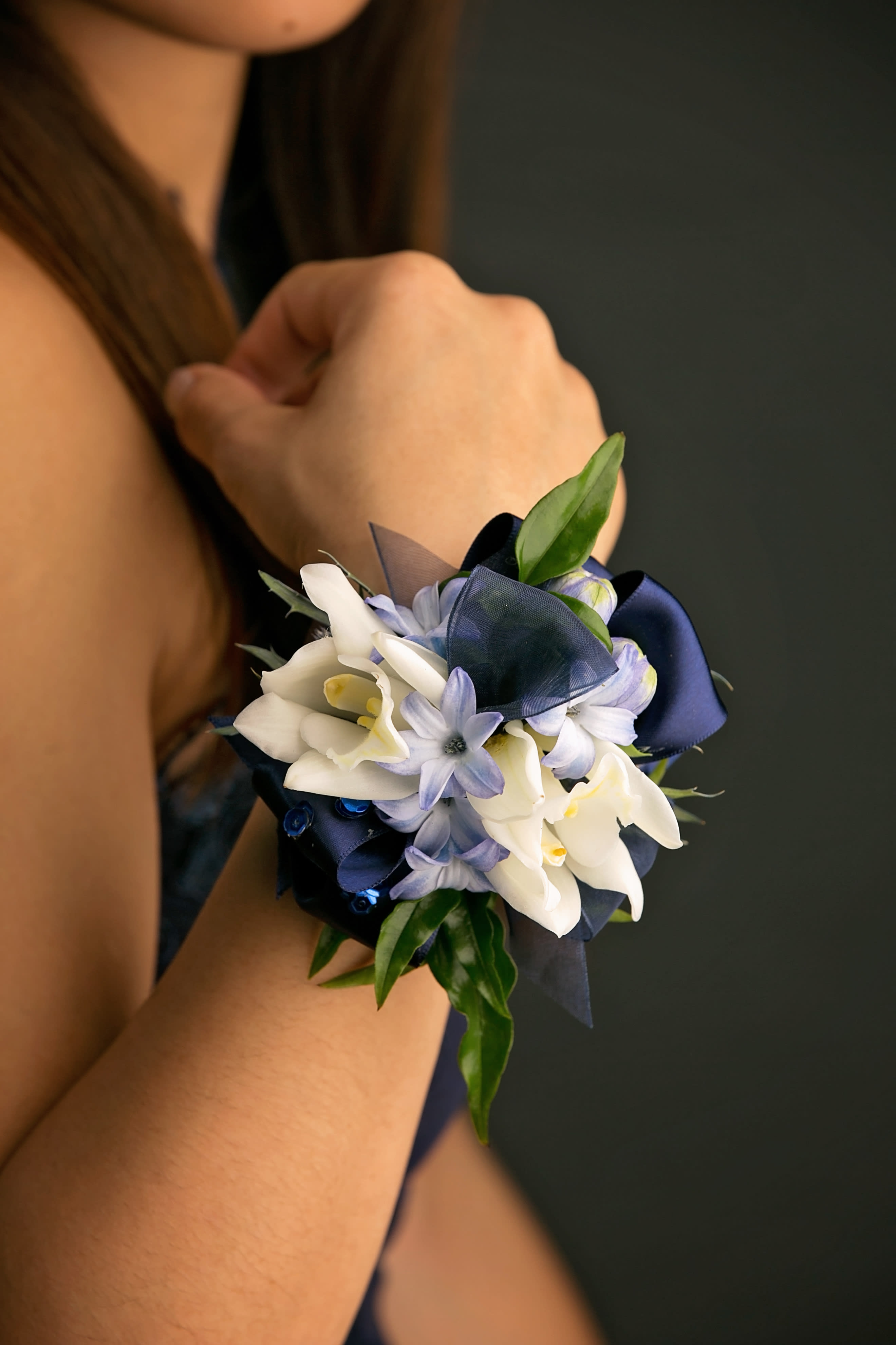 Wrist corsage with white and pale blue flowers and navy ribbon on a person’s arm