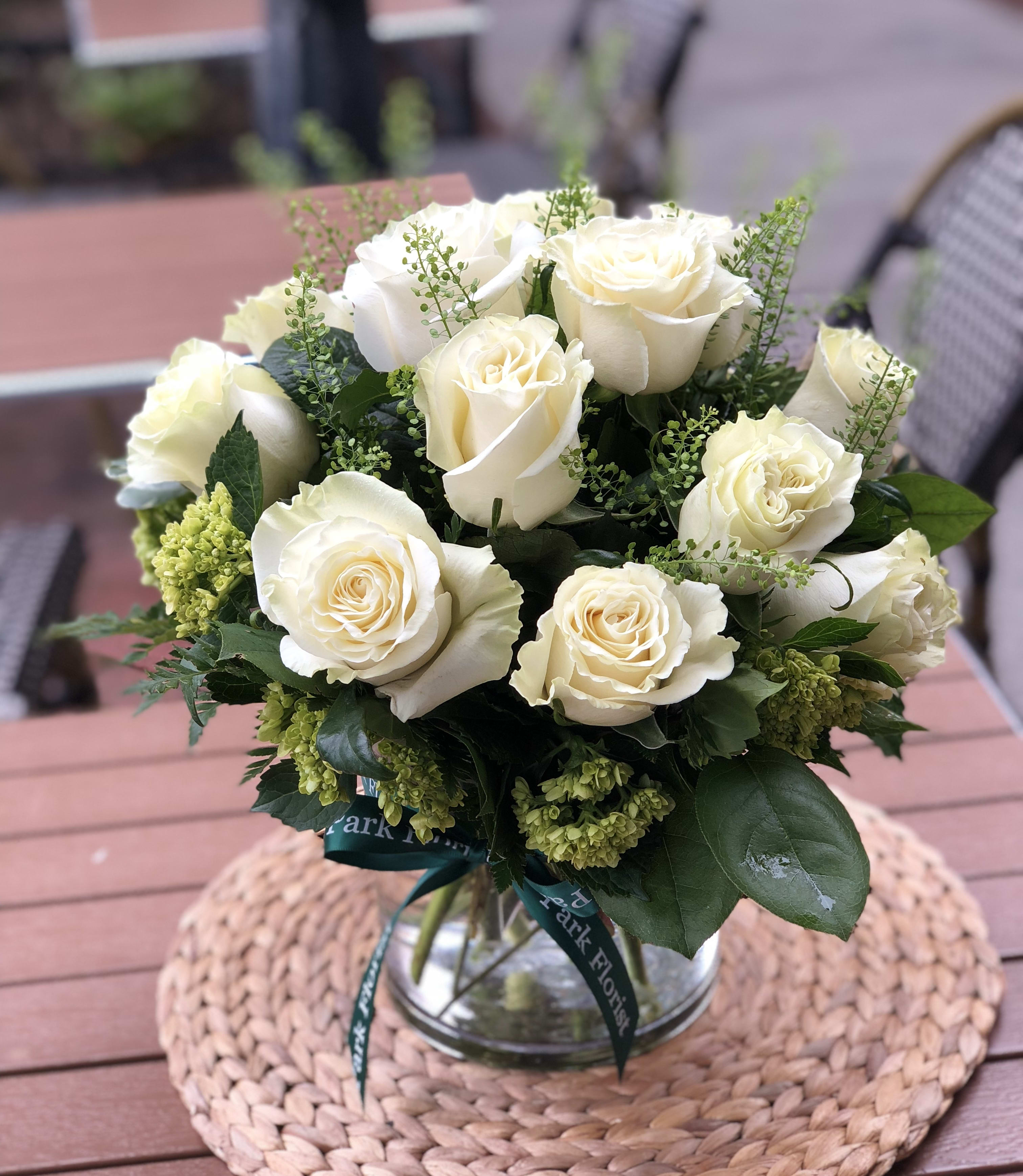 Round bouquet of white roses with green accents in a clear glass vase.
