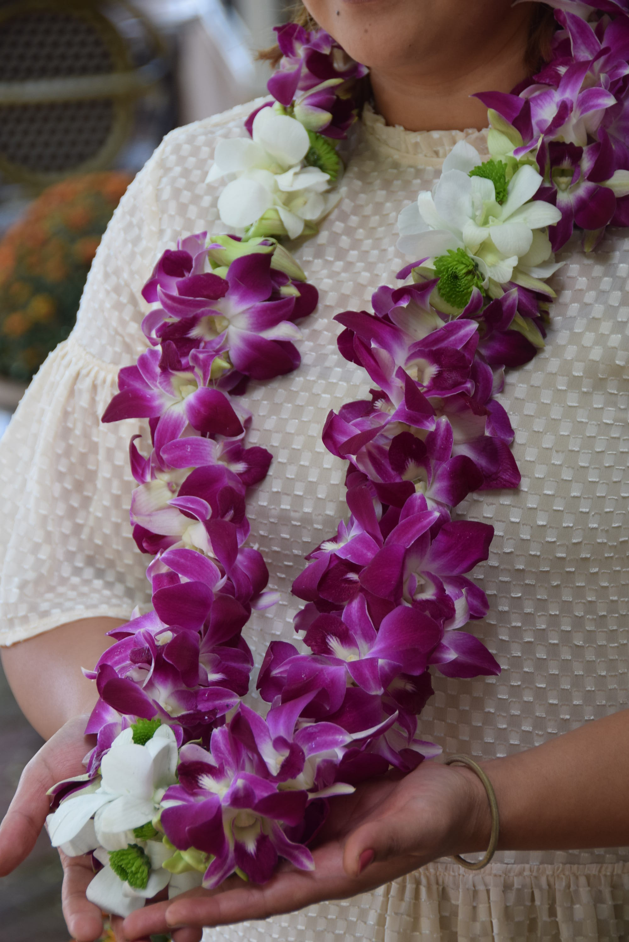 Purple and white orchid lei worn around a person’s neck and held in their hands