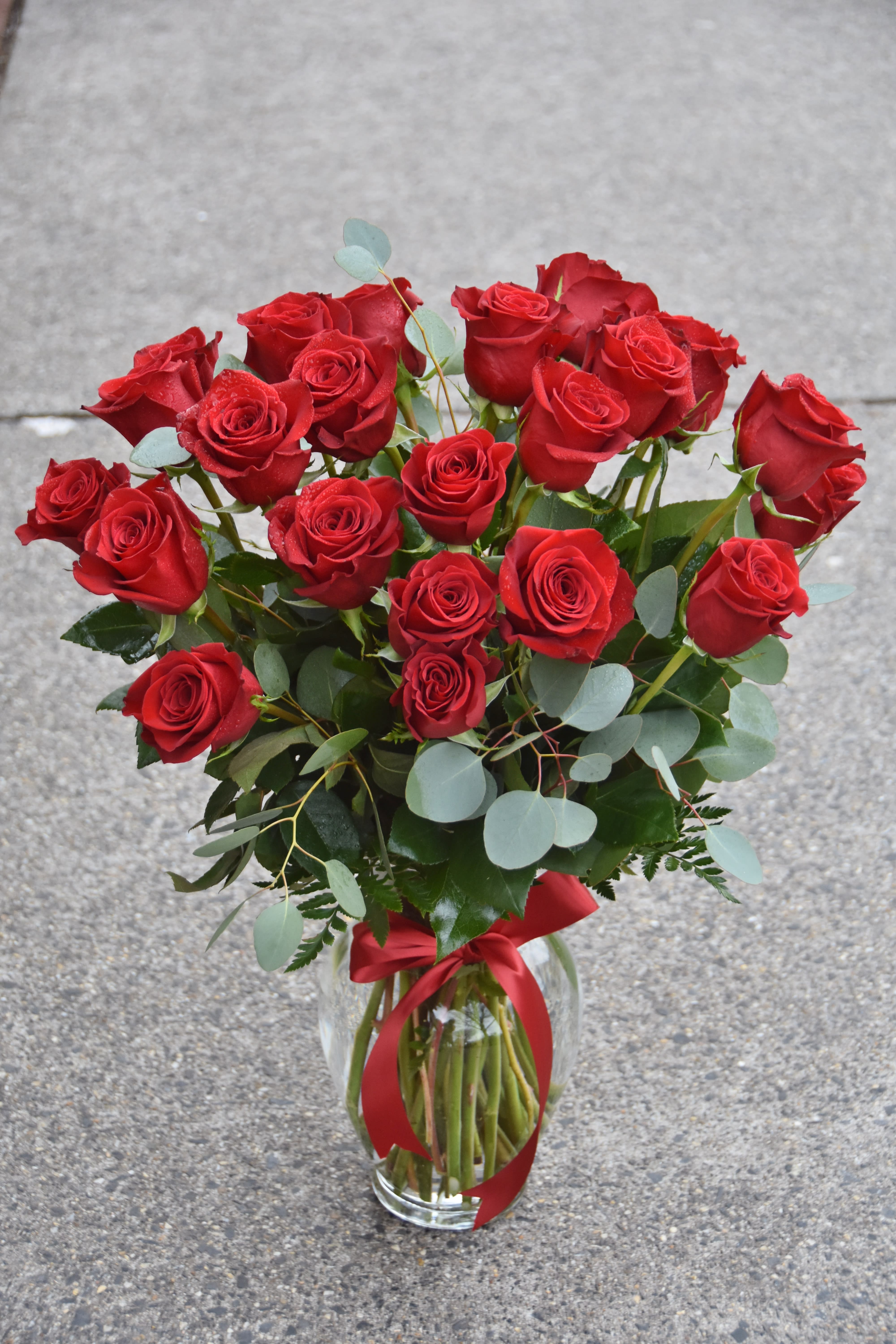 Tall arrangement of long-stem red roses in a clear glass vase with a red ribbon bow