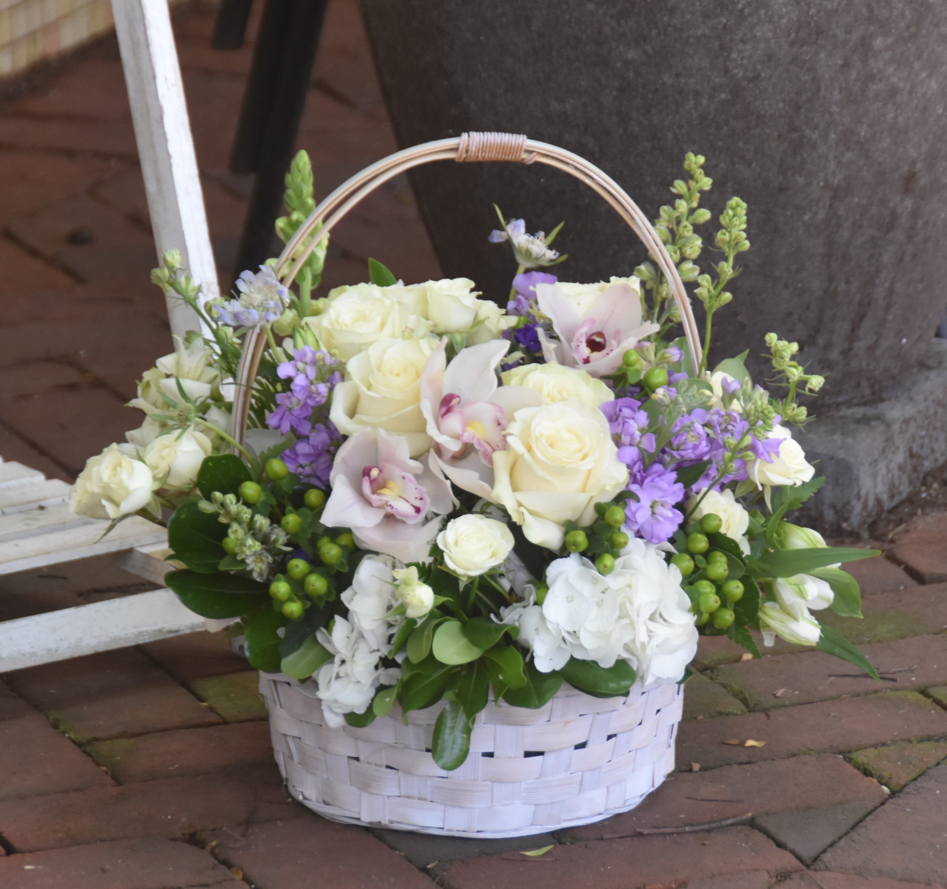 White basket of ivory roses, orchids, and purple flowers with green berries